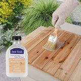 Person applying wood wax oil to a wooden surface with a bottle of Just Teak wood wax oil and a brush.